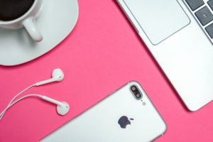 iPhone, earphones, coffee, and laptop on pink background